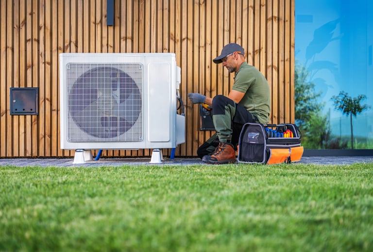 A technician servicing an air conditioning unit beside a modern home
