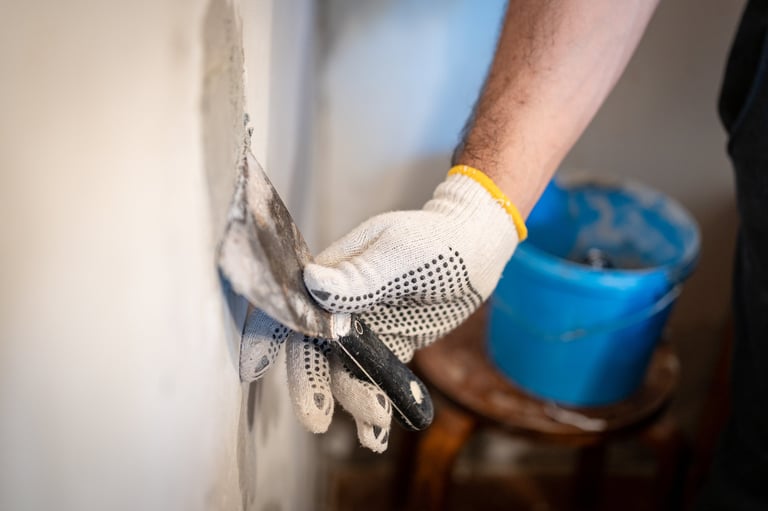 Close-up of a worker's gloved hand using a small putty knife to press thick patching compound firmly into a hole in the interior wall