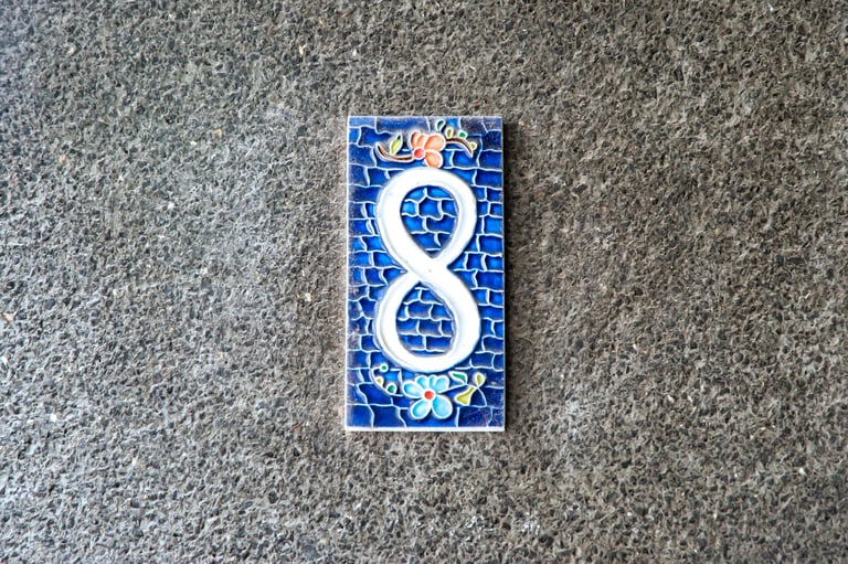 Ceramic number eight tile centered on rough concrete wall with copy space, minimal composition, architectural detail
