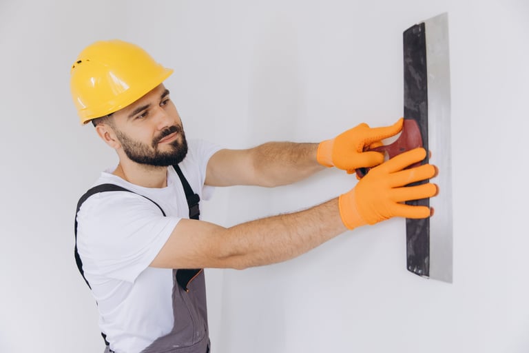 Man in uniform applying plastering compound to a smooth white wall, performing professional repair and home improvement work
