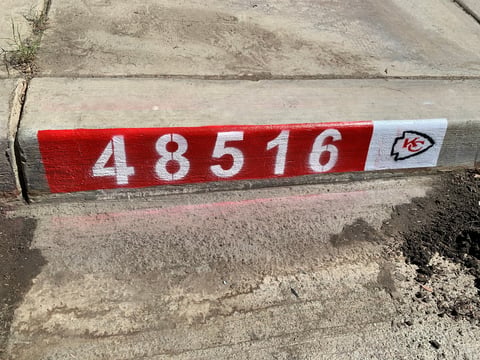 Red and white painted curb with numbers 48516 and Kansas City Chiefs logo on concrete street edge