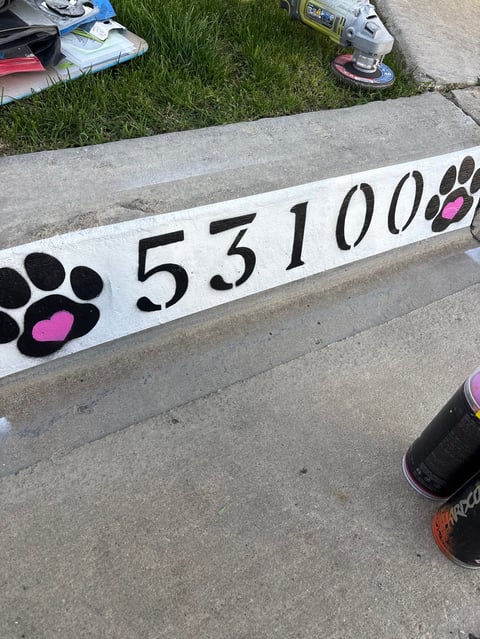 A white board painted with paw prints and the number 531000 in black and pink, resting on concrete