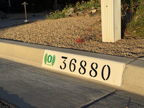 House address number 36880 painted on cream-colored curb with green decorative emblem