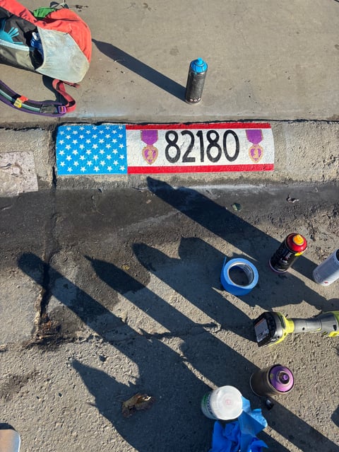 Overhead view of race bib 82180 with American flag design and various sports equipment casting shadows on pavement