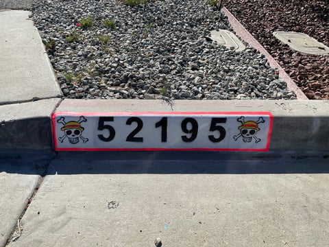 Pink address marker displaying number 52195 mounted on concrete curb with decorative emblems on sides