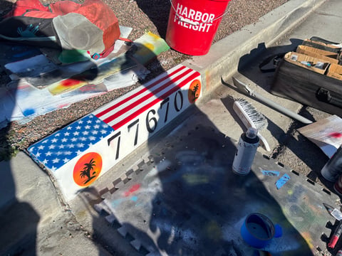 Overhead view of kite-flying equipment including an American flag kite and various gear scattered on concrete ground