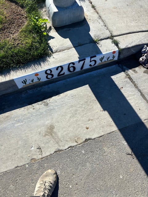 Overhead view of a measurement scale marked 82675 placed on concrete sidewalk with shadows and persons shoe visible