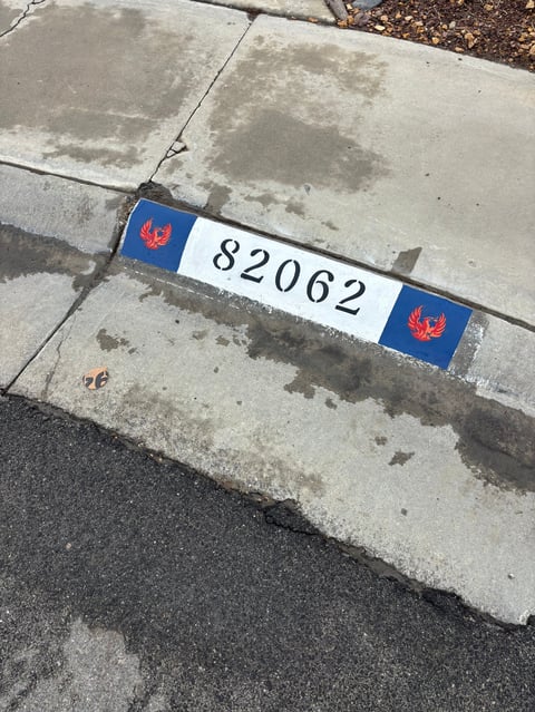 Address marker displaying number 82062 with red phoenix logo on blue and white plate attached to concrete curb