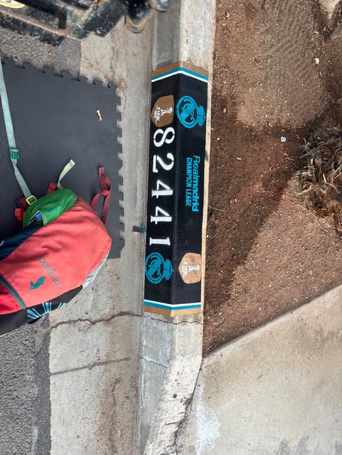 Black vertical sign with blue trim showing number 3241 mounted on concrete wall next to red backpack on pavement