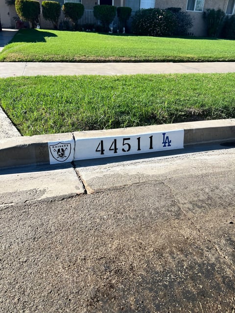 Street curb with address number 44511 and Dodgers logo, green lawn and hedges visible above