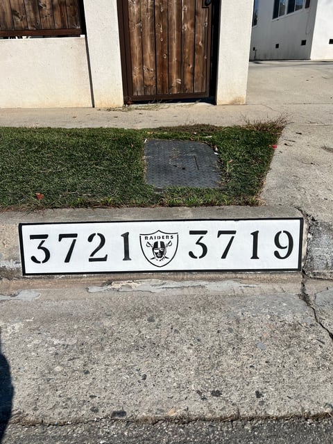 Oakland Raiders curb address marker showing numbers 3721 and 3719 with team logo on concrete pavement