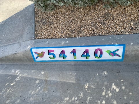 Colorful address marker with numbers 541140 and hummingbird designs on concrete curb